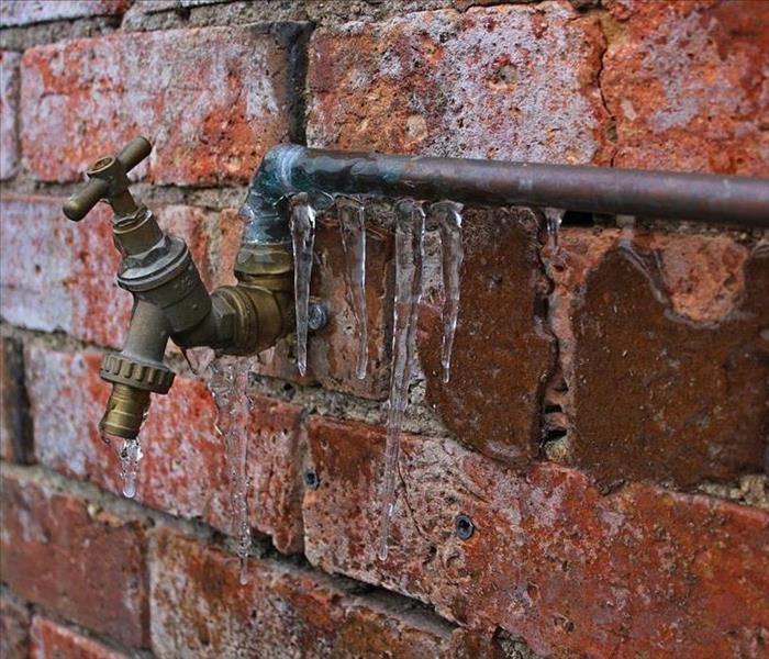 A hose bib on a brick wall, with icicles hanging off of it.