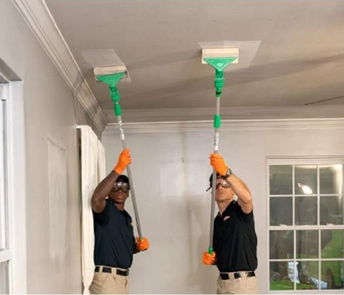 Two SERVPRO technicians cleaning smoke damage off a ceiling.